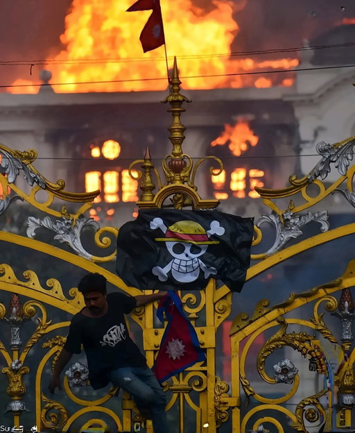Things that should be happening later in the One Piece world are already happening our own world. In Nepal, protesters raised the Straw Hat Pirates’ flag in front of Parliament as the building burned during demonstrations against the government.

One Piece is not just the greatest story ever told it’s inspiring a new generation to rise up for their freedom and protest against corrupt governments. In fact, it has already become a symbolic threat to authority, just as the World Government fears it in the series. If such a government existed in our world, it would feel that same threat today.

In Nepal  mainly by Gen Z, the protests began last week against corruption, inequality, and the social media ban. Thousands gathered at Maitighar, waving both Nepal’s national flag and the One Piece flag to demand reforms.

This had happened earlier in Indonesia too, where protesters marched with the Straw Hat flag during anti government rallies. Now, Nepal has become the second country this year where the symbol of Luffy’s crew is being used as a banner of resistance.