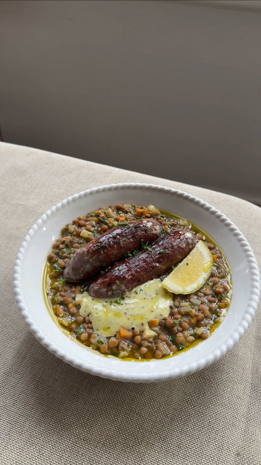 This is exactly the kind of food I love to make for myself, simple, comforting, and full of flavour. The lentils are slow-braised with wine, stock, celeriac and bay until rich and silky, then topped with really good quality butchers’ sausages (these were venison and red wine from @hampsteadbutcher hits every time!

For 2:
1 tbsp olive oil
1 shallot, finely diced
1 carrot, finely diced
1/4 small celeriac, diced
1 bay leaf
200g lentils, I used @belazu_co jarred lentils but puy lentils will work for this
100ml white wine
300ml chicken or vegetable stock
3 tbsp parsley, finely chopped
4 good-quality pork sausages
2 tbsp mayonnaise
1 tsp wholegrain mustard
Slice of lemon to garnish

For the herb oil:
Small bunch chives or dill
60ml olive oil
Pinch of salt

1: First make the herb oil, blend the herbs with a neutral oil and a pinch of salt until vibrant and smooth. Strain with a muslin cloth and set aside.
2. Heat the olive oil in a pan and cook shallot, carrot, celeriac & bay leaf for 10 mins until soft and lightly golden.
3. Stir in the wine and let simmer off for 2 mins then add the lentils and stock, cook gently for 20 mins then stir in your parsley in the final few mins 
4. Meanwhile, heat olive oil in a pan and cook your sausages
5. Mix the mayo with the mustard and 4-5 tbsp herb oil
6. Remove bay leaf from lentils and season to taste. Spoon the lentils onto plates, top with sausages, add a dollop of the herby mustard mayo on the side and garnish with a slice of lemon