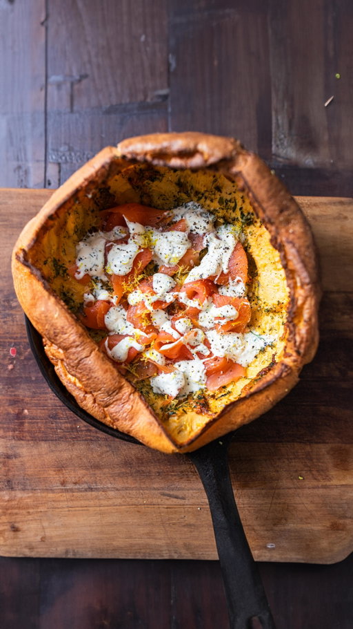 It’s that time of year again! The Smoked Salmon Savoury Dutch Baby.

Great for Christmas morning, Boxing Day or New Year’s Day.

4 eggs
180g milk
90g plain flour
1/4 tsp salt
40g butter
20g parmesan cheese
15g fresh parsley, dill & tarragon
1 garlic clove

To serve

200g smoked salmon
50g crème fraîche
2 tsp fresh dill
1 tbsp lemon juice
1 tsp lemon zest
1/4 tsp salt

Preheat your oven to 230°C (445°F) and place your cast iron pan on the middle shelf. Make sure there’s enough space above it for your Dutch Baby to expand.
In a stick blender jug add the eggs, flour, milk & salt. Blend until smooth and aerated. This can also be done in a stand up blender.
Leave the mixture to stand whilst the oven comes up to temperature. The closer the mix is to room temp, the better rise you’ll get in the finished product.
Grate the parmesan, chop the herbs fine and mince the garlic. Transfer to a bowl. I like to add a pinch of salt to this mixture also.
When you’re ready to go, remove the pan from the oven and add the butter. Let it bubble and melt down completely. Then pour your batter mix into the pan.
Scatter the cheese and herb mix over the top and return to the oven for 15 to 20 minutes. Do not open the oven during this time.
To serve

In a bowl mix the crème fraîche, chopped dill, lemon juice, lemon zest and salt.
Arrange the smoked salmon in the bottom of the Dutch Baby and spoon over the dill crème fraîche.

A few notes:

- Get the batter to room temperature before cooking to get a good rise.
- That is an obscene amount of butter :) You don’t really *need* that much (the recipe on my site is correct) but it’s only Christmas once!
- Yes, it’s one pan because I didn’t include the blender jug.
- Isn’t this just a huge Yorkshire pudding? Call it whatever makes you happy. 
- What’s Dutch about it? Nothing. The name comes from an American misunderstanding of ‘Deutsche’ because it’s based on a German pancake.
- The pan doesn’t have to be cast iron, just one that can go in the oven. That includes similar sized and shape cake tins.
- How does it rise without yeast? Steam!