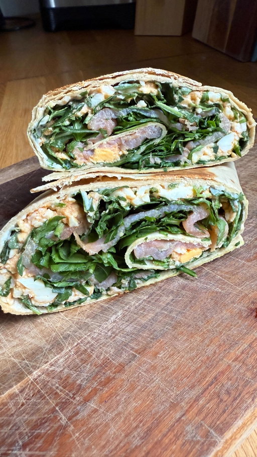 Wrap de Salmão com Paté de Ovo cremoso 😋 Guarda já e diz-me se ficaste com vontade de experimentar! 

Ingredientes
2 wraps de trigo
2 queijinhos A Vaca que Ri
Rúcula a gosto
2 ovos cozidos
1 colher de sopa de iogurte grego natural light
1 colher de chá de sal
1 colher de chá de pimentão doce
3 fatias de salmão fumado

Processo:

Coloca os dois wraps na bancada, sobrepondo cerca de um terço de um sobre o outro, para criares uma base maior e mais firme.
Barra os queijinhos A Vaca que Ri (light) pelos wraps. Por cima, adiciona um pouco de rúcula.
Numa taça, coloca os ovos cozidos e esmaga bem com um garfo até ficarem em migalhas pequenas. Junta o iogurte grego, o sal e o pimentão doce e mistura tudo até obteres um patê cremoso.
Espalha esse patê sobre os wraps. Adiciona mais um pouco de rúcula, distribui as fatias de salmão fumado e finaliza com mais um pouco de rúcula.
Enrola bem apertado, formando um wrap grande.
Leva a uma frigideira antiaderente, em lume médio, e deixa dourar de um lado e do outro até ficar ligeiramente crocante por fora.
Retira, deixa arrefecer 1–2 minutos, corta ao meio e está pronto a comer ou a embrulhar para levar.