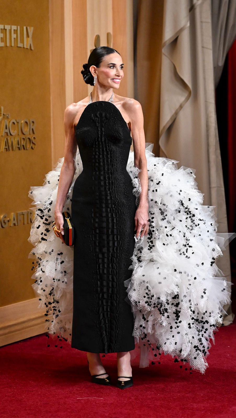 @DEMIMOORE WEARS A SCHIAPARELLI HAUTE COUTURE DRESS BY @DANIELROSEBERRY AT THE 32ND ANNUAL SCREEN ACTORS GUILD AWARDS IN LOS ANGELES. 

A look that required over 7 700 hours of embroidery work: its white tulle cloud at the back is embroidered with 8500 black mimosas in silk thread and over 11000 crystals.
The bustier dress in black wool crepe is embellished with a satin-stitch trompe l’œil crocodile tail at the front, paired with black satin mule with an asymmetrical wavy vamp embellished with a gold metal Keyhole bijoux. 

Stylist: @bradgoreski 

#Schiaparelli #DemiMoore