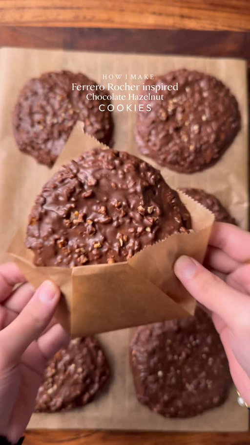 Ferrero Rocher inspired chocolate hazelnut cookies🤤. Ferrero Rocher vibes in every bite, Rich chocolate, crunchy hazelnuts, and that melt-in-your-mouth magic.

INGREDIENTS:
•115g cold chopped unsalted butter
•80g caster sugar
•80g light brown sugar
•238g plain flour 
•½ tsp salt
•1 & ½ tsp baking powder
•¼ tsp baking soda
•1 whole egg + egg yolk 
•½ tsp vanilla
•250g Cooking or Milk chocolate 
•1/2 cup Chopped and roasted hazelnuts 
•Nutella and hazelnut spread 
INSTRUCTIONS:
•Cut cling wrap into small squares. Scoop ½ teaspoon Nutella and Scoop ½ teaspoon of Hazelnut spread onto individual cling-wrap squares. Fold to seal and freeze until solid. (Repeat for however many stuffed cookies you plan to make.)
•In a large mixing bowl, add the cubed butter and whisk until slightly creamy. Add the white sugar and light brown sugar, then whisk together until well combined and fluffy.
•Add the eggs, vanilla extract. Whisk until fully incorporated.
•Add the flour, baking powder, baking soda, and salt. Gently mix until just combined, do not overmix.
•Portion the dough into 65g-70g balls. Press a frozen Nutella hazelnut piece into the centre of each dough ball, seal well, and roll into a smooth ball.
•Place the cookie dough balls onto a tray and freeze for at least 1 hour (or overnight for best results).
•Preheat oven to 175-180C (350°F). Bake for 10-15 minutes or until the tops are lightly golden while the centres remain soft.
•Remove from the oven and let cool.
•Melt the cooking or milk chocolate using double broiler method and add chopped & roasted hazelnuts in it. 
•Spread a layer of melted chocolate–hazelnut mixture onto baking paper, just enough to coat the base of the cookie. Gently place the cooled cookie on top, then spoon more of the mixture over it, making sure the cookie is fully covered and evenly coated.
•Let the chocolate mixture set completely before serving, Enjoy! 
NOTE: Store any extra dough balls in an airtight container or freezer bag and freeze for later. Whenever a cookie craving hits, bake straight from frozen🫶🏻

#cookie #ferrerorocher #fyp #explorepage #chocolate