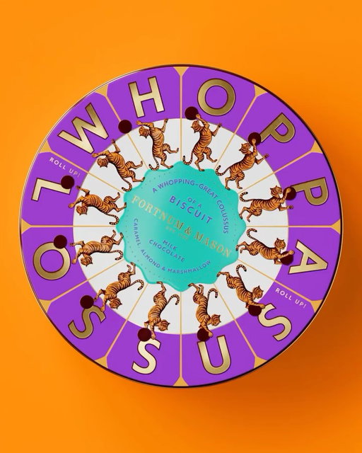 Courtesy of Design Bridge, Fortnum and Mason’s Whoppalossus comes housed in large, circular tin with a purple and gold outer ring spelling its namesake in oversized individual letter blocks. The center of the lid features a ring of illustrated tigers in full stride, in a style that pulls directly from Fortnum and Mason’s long tradition of decorative illustration. 

A teal blob shape at the center highlights the product description, creating a deliberate contrast between the exuberant outer ring and a more refined inner moment.