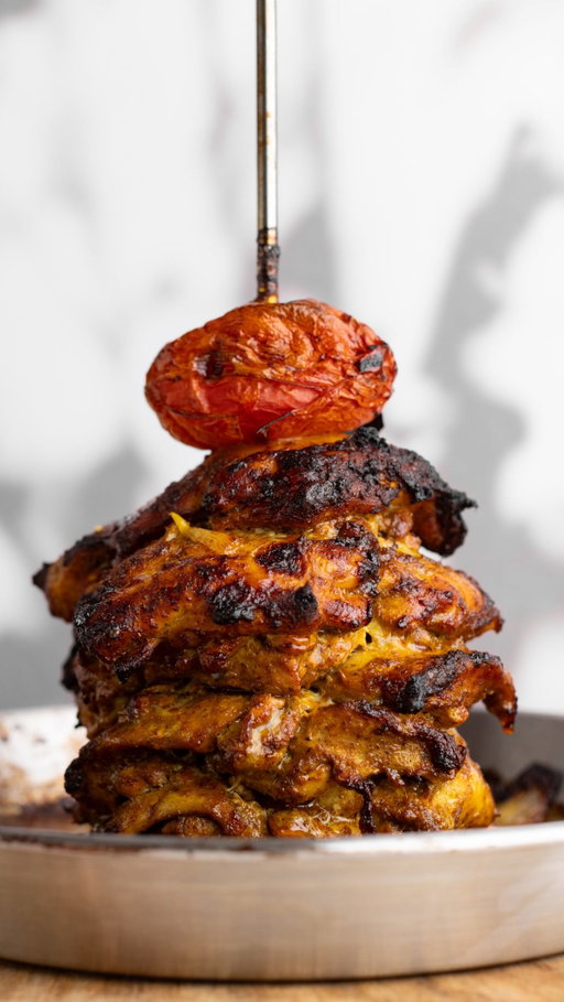 Middle Eastern flavor, straight off the spit. Juicy Chicken Shawarma kicks off Episode 1 of No Passport Needed where we make global street food accessible at home from @theboldappetite 🍗

- 1 tsp ground cumin
- 1 tsp ground coriander
- 1 tsp onion powder
- 1 tsp cayenne pepper
- 1 tsp Spanish paprika
- 1 tsp sweet paprika
- 1 tsp turmeric
- ½ tsp dried oregano
- ½ tsp allspice
- ¼ tsp ground cardamom
- 3½ lbs boneless, skinless chicken thighs
- 1 tsp tomato paste
- 5 garlic cloves, grated
- 1 lemon, juiced
- ¼ cup olive oil
- Kosher salt
- 1 Roma tomato
- 1 white onion, roughly chopped

1. Combine the spices in a small bowl
2. Place the chicken thighs in a large bowl, and add the tomato paste, grated garlic, lemon juice, olive oil, spice mixture, and a heavy pinch of kosher salt (approx. ½ tsp).
3. Mix thoroughly and marinate in the fridge—preferably overnight, or at least 1 hour.
4. Preheat the oven to 400°F/200°C.
5. Layer the chicken on the at-home vertical spit, rotating each thigh to ensure an even stack.
6. Place the tomato on top and scatter the roughly chopped onions at the bottom. Depending on the thickness of the thighs, roasting can take anywhere from 1 hour to 1 hour and 20 minutes. Every 20 minutes, baste the chicken with the rendered juices. Roast until fully cooked through (165°F).
7. Once done, remove from the oven, and shave the chicken off the spit.
8. Serve in a pita or laffa with your choice of suggested toppings below.
(While an at-home spit is recommended, the chicken can also be grilled (8-12 minutes) or roasted on a sheet pan (18-20 minutes).)
