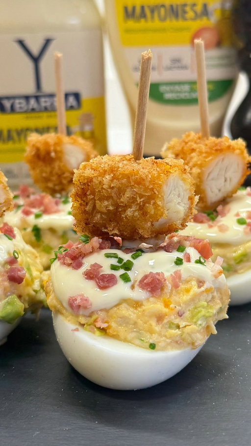 Publi.😋Huevos rellenos estilo César!

Al loro porque hoy hemos fusionado dos clásicos del veranito en un solo bocado: huevos rellenos + ensalada césar = Una combinación cremosa y súper rica con bacon crujiente, el toque del parmesano, pollo empanado y mayonesa de @grupoybarra Y sí, saben incluso mejor de lo que te esperas leyéndolo. Con estos huevos rellenos vas a triunfar este verano porque son muy originales y encima están buenísimos. Ya me contarás!
•
INGREDIENTES:
5 huevos
100 grs. pollo asado
50 grs. bacon
15 grs. parmesano
30 grs. lechuga o cogollo
4 cs. mayonesa @grupoybarra
Pimienta negra
•
En primer lugar, cuece los huevos 9 minutos, pela, corta a la mitad y retira las yemas. Frie el bacon, deja enfríar. Mientras, ralla el queso parmesano. Aprovecha algún trozo de pollo asado que te haya sobrado (o también lo puedes hacer con filetes de pechuga a la plancha) y trocéalos finamente, al igual que el bacon y la lechuga. En un bowl amplio pon todos ingredientes troceados junto con las yemas cocidas, un toque de pimienta negra y las cucharadas de mayonesa.
•
Mezcla todo bien hasta que esté bien jugoso, entonces rellena las mitades de los huevos cocidos (yo he utilizado una cuchara de helado para darles más volumen, pero puedes hacerlo con una cuchara sopera). Napa ligeramente con un poquito de mayonesa, unos trocitos de bacon y cebollino fresco picado para darle frescor. Termina colocando un palillo con un troco de pollo empanado (una porción de fingers de pollo o pechuga). Ya te digo yo que vas a triunfar.
