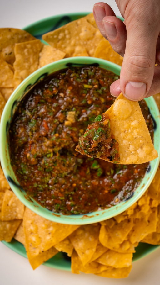 Salsa Roja

Ingredients

- 5 Plum tomato
- 1/3 white onion, skin on
- 2 Jalapeños
- 2 cloves garlic, skin on
- 1 bunch coriander
- 1 lime, juice
- salt to taste

Method

1. Slice the tomatoes in half, lengthwise. 
2. Slice the Jalapeños in half lengthwise and leave the seeds in or out, depending on how spicy you like it. 
3. Place a large cast iron or heavy based pan over high heat, without oil. Place all the vegetables on the pan, skin side down to char for 5-6 minutes. You can achieve a similar result with tray in a hot oven or boiler. The key is to evenly char the vegetables until they dark and cooked through.
4. Once you have a dark char on one side, flip them over for a further 2-3 minutes. Once the vegetables are cooked, place them into a food processor. Remember to remove the skin from the garlic and onion before blending on high for 30 seconds with a pinch of salt. If you don’t have a food processor you can use a chopping board and a knife or better yet a Molcajete. 
5. Add the coriander with the juice of a lime and salt to taste. Continue blending until the coriander has become roughly chopped through the salsa. Serve with a big bowl of corn chips and enjoy.