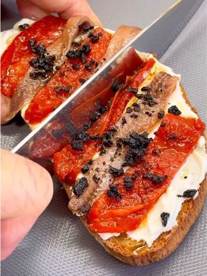 ¿Cenamos una tosta diferente?😋👌🏻 Ricotta con un toque de limón, piquillos salteados, anchoa y esa “tierra” de aceituna negra que cruje y te remata el bocado. Una mezcla perfecta: cremoso, cítrico, dulce, salado y crujiente. Nada complicado, pero con ese puntito de restaurante en casa. Pruébala y luego me dices si no te ha hecho sonreír.😜 • INGREDIENTES: 5 pimientos piquillo 200 grs. queso ricotta (o queso crema) Ralladura limón Pimienta negra Anchoas en aceite Aceitunas negras Rebanadas de pan AOVE • Corta las rebanadas de pan, echa un poquito de aceite y lleva al horno a 200º hasta que estén tostadas. Prepara la mezcla de queso ricotta o queso crema con ralladura y zumo de limón y un poco de pimienta negra, reserva. Ahora, saltea a fuego fuerte unos buenos pimientos de piquillo dora por ambas caras y córtalos en tiras.  • Por último, corta unas aceitunas negras por la mitad, seca muy bien y lleva al micro (máxima potencia) unos 4 mins para que se deshidraten bien. Ponlas en un procesador de cocina y tritura hasta obtener la “tierra” de aceituna negra. Para el montaje, unta una capa generosa de la mezcla de queso en la tosta, ve alternando tiras de pimiento de piquillo con anchoas en aceite y termina espolvoreando la tierra de aceituna por encima… brutal! • Tienes la opción de hacer una variante con boquerones en vinagre y cebollino fresco picado, así tus invitados podrán elegir entre las dos… a cada cual más rica!