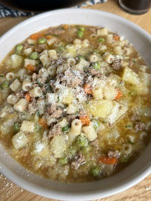 How does your family make minestra? Minestra con Carne Macinata (Italian Beef and Potato Soup)  This is one of those humble Italian soups you make when you want something hearty without overthinking. It’s the classic clean out the fridge soup every Italian family knows or the nothing in the fridge so make a soup kind of meal. As a kid I never understood why minestra was always a weeknight dinner and now it makes sense. It works, but most importantly it’s easy to make and tastes like home regardless of what is in it.  Ingredients: 1 lb ground beef 1/2 lb pasta  2 potatoes, cubed 1 carrot, diced 1 onion, diced 1 clove garlic 1/2 cup fresh peas 1/2  cup tomato purée Fresh parsley, chopped Olive oil Salt & freshly ground black pepper Vegetable broth or water (enough to cover) Grated cheese Directions:  1. Warm a generous drizzle of olive oil in a large pot. Add the onion, carrot and garlic. Sauté until the vegetables soften. 2. Add the ground beef and break it apart with a wooden spoon and cook for a few minutes.  3. Stir in the tomato purée and season with salt and black pepper. 4. Add the potatoes and pour in enough vegetable broth (or water) to fully cover everything. Bring to a gentle simmer, cover, and cook for 20 minutes. 5. After 20 minutes, check the liquid level and add more if needed. Add the pasta and the peas directly into the pot.  6. Cook for 8 to 10 minutes, stirring occasionally so nothing sticks. 7. Finish with fresh parsley and a light sprinkle of grated cheese.  Pour a glass of @Gratsi Wine Red and let simple flavors warm you up. Buon Appetito! #soup #EasyRecipe #fy 