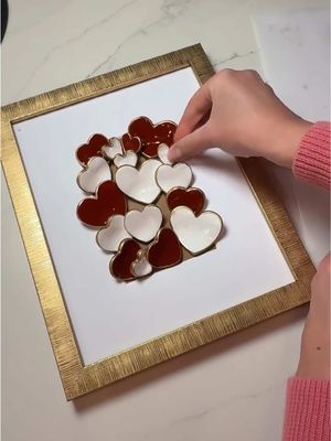 Started with air-dry crayola clay, heart shaped cookie cutters, letting them dry on a paper plate to create the perfect curved shape. I painted them crimson and white with acrylic paint, added gold pin trim on the smooth edges for extra pop and pizzazz, then removed the glass from a budget frame and glued the hearts directly onto the mat for a fun 3D pop-out effect. I love putting a creative spin on DIY crafts, turning simple supplies into personalized home decor and a work of art with lots of beauty and character. #fyp #art #valentines #handmade #artist