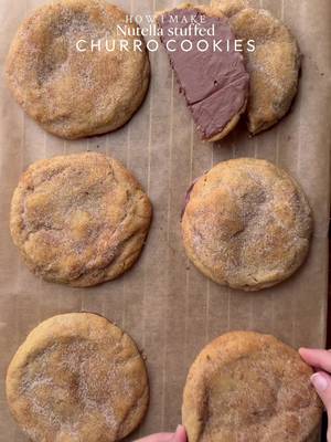 Yields: 6-7 Cookies  INGREDIENTS: FOR COOKIES •115g chopped unsalted butter •80g caster sugar •80g light brown sugar •238g plain flour  •1 tsp cinnamon powder  •½ tsp salt •1 & ½ tsp baking powder •¼ tsp baking soda •1 egg + egg yolk  •½ tsp vanilla •Nutella  FOR COATING: •150g Chocolate bar •50g caster sugar  •2 tsp cinnamon powder INSTRUCTIONS: •Cut cling wrap into small squares. Scoop 1 tsp Nutella spread onto individual cling-wrap squares. Fold to seal and freeze until solid. (Repeat for however many stuffed cookies you plan to make.) •In a large mixing bowl, add the cubed butter and whisk until slightly creamy. Add the white sugar and light brown sugar, then whisk together until well combined and fluffy. •Add the eggs, vanilla extract and Whisk until fully incorporated. •Add baking powder, baking soda, and salt and mix everything together and then in a separate bowl mix flour and cinnamon powder together and add it into the batter, gently mix until just combined, do not overmix. •In a separate bowl mix cinnamon powder and sugar together and keep it aside. •Portion the dough into 85-90gballs. Press a frozen nutella spread piece into the centre of each dough ball, seal well, and roll into a ball. Coat the dough ball with cinnamon sugar mixture and place it on a baking tray. •Preheat fan oven to 175-180C (350°F). Bake for 10-15 minutes or until the tops are lightly golden while the centres remain soft. •Remove from the oven and let it cool. At this point you can coat the cookie again with cinnamon sugar mixture. •Now melt the chocolate bar using double broiler method and coat the bottom of each cookie with melted chocolate and keep it aside to set. •Enjoy✨ NOTE: Store any extra dough balls in an airtight container or freezer bag and freeze for later. Whenever a cookie craving hits, bake straight from frozen🫶🏻 #cookie #nutella #churros #dessert #chocolate 