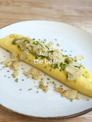 MY TOP 3 DISHES FROM THE BEAR 🐻🧑🏻‍🍳 #2 - Sydney’s Omelette 🥚🍳   FULL RECIPE BELOW ⬇️  INGREDIENTS: 4 large eggs 3 tsp butter (in 3 cubes) Pinch of fine sea/kosher salt 1 x shallot & chive Boursin, in a piping bag 1/4 bunch chives 1 handful sour cream & onion chips INSTRUCTIONS: 1. Crack your eggs into a fine mesh strainer placed over a bowl. Whisk your eggs with a fork until fully smooth. The eggs will naturally start to fall through the holes in the strainer. Use a spatula to push the egg through the strainer if needed. Season your eggs with salt. 2. Heat a good quality, 24cm non-stick pan over medium-high heat. Add 2 tsp butter, and once it’s fully melted, add your eggs. 3. As soon as your eggs hit the pan, turn the heat down to low, and scramble vigorously. I like to gently shake my pan, while making a smaller circular motion with my spatula, moving counter-clockwise around the pan while doing so (this might sound complicated - but the video will help demonstrate!). 4. Once the eggs have started to set, and the edges of your eggs are cooked, leave your omelette without touching it, to continue cooking 1-2 more minutes. Release the very outer edge of the omelette from the walls of the pan, so it doesn’t dry out. Once the eggs are 3/4 of the way cooked, and the top of your omelette is slightly wet to the touch (see video), you can add your Boursin. Turn off the heat on your pan, and pipe the Boursin in a straight line about 1/4 of the way into the eggs, closest to you. 5. With a plate ready, starting from the handle, make 2-3 quarter folds on your omelette, and jerk your pan so that the unfolded part sits on the rim of the pan (opposite the handle). Then, in one motion, “flop” the omelette onto the plate, finishing the last fold. If your omelette is not immediately beautiful - not to worry! You can shape it with your fingers or a paper towel. 6. Brush your omelette with your remaining 1 tsp of butter, garnish with chives & chips, and enjoy!  #thebear #omelette #Recipe #homecooking