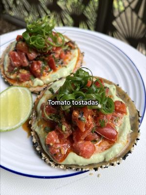 Sesame crusted tostadas with marinated tomatoes 🍅 She's not traditional, in fact she doesn't even know what she is but I promise you're gonna have a good time!! There's buckets of flavour and barely any cooking so whack this one in the pocket of your favourite jorts for a hot summers day. RECIPE (for 2-4 tacos) 325g beef tomatoes, cubed and salted 1 tbsp plain flour 2 tsp water 4 small corn tortillas 50g sesame seeds 40g black sesame seeds 1 tbsp soy sauce ¼ lime, juice 1 tbsp sesame oil Pinch caster sugar 1 tbsp coriander, finely chopped 1 tbsp chilli oil ¾ tbsp vegan mayo  1 spring onion, thinly sliced 1 tbsp nori, thinly sliced ½ carton silken tofu ½ avocado Salt Lime juice, to taste 1. Place the diced tomatoes in a sieve over a bowl and salt with a pinch of salt. Leave to sit for 10 minutes to drain excess moisture. 2. Mix the flour and water to make a paste. Brush the paste over one side of the tortillas then place down in a mix of the black and white sesame seeds. Shallow fry, bake or air fry until crispy. 3. Mix the drained tomatoes with all the ingredients for the sauce. 4. Blend the avocado and silken tofu with a squeeze of lime and a pinch of salt. 5. Serve the crispy tortillas with the whipped tofu and avocado sauce then top with the tomatoes, drizzle with some of the leftover marinade and top with spring onion greens. Enjoy!! #tomatoseason #tostadas #veganrecipe 