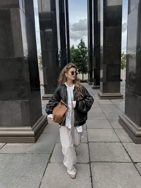 Effortless street style outfit featuring striped pajama pants, an oversized black leather jacket, a white layered shirt, brown suede shoes, sunglasses, and a structured tan leather bag. A chic way to wear pajama pants outside the house, perfect for casual fall outfits, transitional weather style, minimalist fashion, Scandinavian style, elevated basics, how to style pajama pants, how to wear a leather jacket, wide-leg pants outfit, and effortless city looks. #fashioninspo #falloutfits #styleinspo #hairstyle 