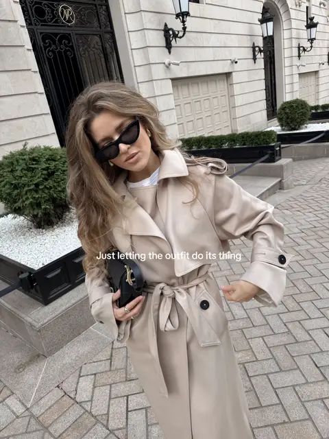 A long beige belted trench coat layered over a simple white top, paired with black loafers and white crew socks. A structured black leather handbag with gold hardware and sleek black sunglasses complete the look. Voluminous soft curls add a feminine, polished touch. Serena van der Woodsen vibe, elegant preppy, quiet luxury, sophisticated, effortless, Gossip Girl aesthetic.