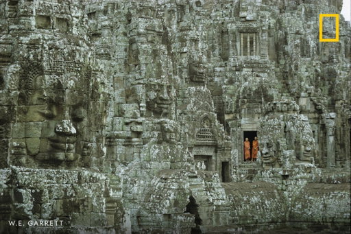 Buddhist monks stand amidst the towering stone faces of the Bayon Temple at Angkor Thom, Cambodia. 